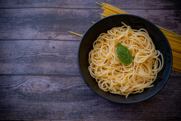 Bowl of cooked spaghetti on top with fresh basil leaf isolated on wooden background, top view.