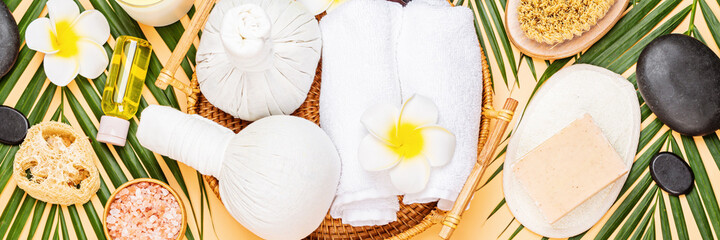 Canvas Print - Spa massage Aromatherapy body care background. Spa herbal balls, cosmetics, towel and tropical leaves on orange table. Top view, flat lay, overhead. Beauty and health care concept