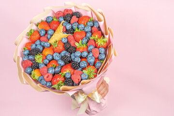 Wall Mural - Edible bouquet of fresh berries, blueberries, raspberries, strawberries, hedgehog in hand on a pink background. There is a place for the text Concept of a useful gift, congratulations on the holiday.