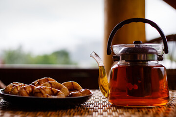 Close up of glass teapot with hot herbal tea and cookies on table.