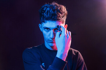 Young barber with work equipment standing in the studio with neon lighting