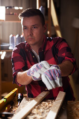 Young male carpenter working in workshop. Carpenter putting on protective gloves.