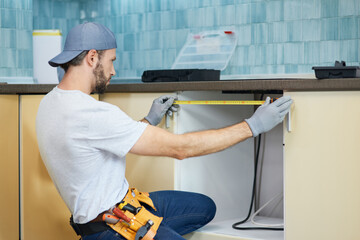 Wall Mural - Young repairman, professional plumber using measure tape while doing plumbing work in a new flat after repair