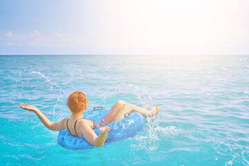 Red-haired girl splashes water. Beautiful young woman resting on an inflatable ring in the sea water. Summer holidays. Cheerful woman with a swimming balloon.