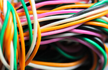 A Bundle Of Multicolored Electrical, Car, Computer, Telephone Wires Twisted Together Background. Orange, Green, Pink, White Cables On Grey Background . Computer Networks, Electrician Services Concept.