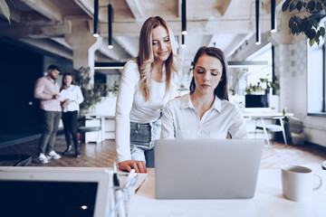 Two young female colleagues discussing business project together in office