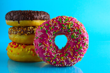 Wall Mural - A still life eating sweet donut berliners in a pink glaze with a colored sprinkler stands next to a stack of doughnuts on a blue bright background with a place to text a picture for the table