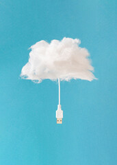 Minimal composition with soft fluffy cloud and computer connection cable against sky blue background. Creative cloud storage symbol.