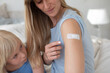 Mother and daughter sit opposite each other and both show the patch on your upper arm after the injection or vaccination and are satisfied.