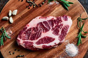 raw pork steak with lard layers is ready for cooking, lies on a wood board with garlic, rosemary, salt and peppercorns. future meat appetizing dish, top view