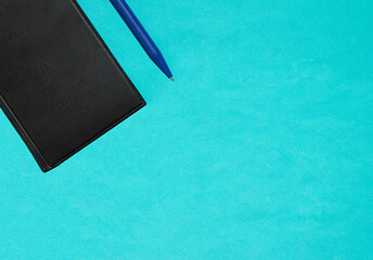 Black notebook and blue pen on a blue background