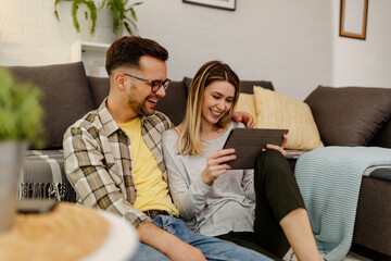 Happy couple with tablet, shopping online, making internet order sitting at home floor.