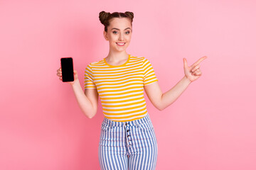 Poster - Photo of optimistic nice brunette lady point empty space hold telephone wear t-shirt pants isolated on pink background