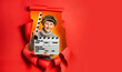 © Olha - Little boy in knitted sweater and retro cap is playing movie maker holding wooden director's clapper board. Child is standing in hole in torn red paper wall. Side spot for your advertising, events.