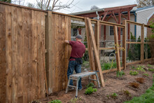 A White, Middle-aged Gay Man Builds A Wooden Fence In His Back Yard.