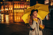 © Zamrznuti tonovi - Beautiful woman using a smartphone and holding a yellow umbrella