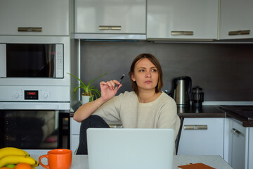 Positive and dreamy female writer working on love roman in home kitchen. Creative process during self-isolation and quarantine. Learning new professional skills, remote work.