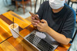 © Quang - Woman wearing protective mask while sitting at coffee shop and using smartphone