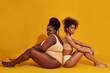 © Svitlana - Full length shot of two diverse african american women in underwear with different body size sitting back to back isolated over yellow background
