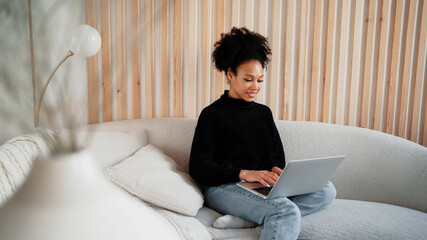 Works at home online makes a new project on the computer. Designer student female afro appearance. Freelancer remote communication with colleagues. Clothing for working in a coworking space.