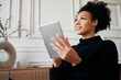 © muse studio - Works at home online makes a new project on a tablet. Freelancer remote communication with colleagues. Designer student female afro appearance. Clothing for working in a coworking space.