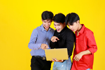 3 adults asian handsome men standing and 1 of them hold laptop on hand. Them look at laptop while feel excited with something on laptop. Shooting in studio with isolated yellow background