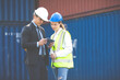 © NVB Stocker - An officer from the Customs Department inspects the cargo in the container yard. Business man in hardhat helmet and caucasian woman foreman worker discuss togetherness