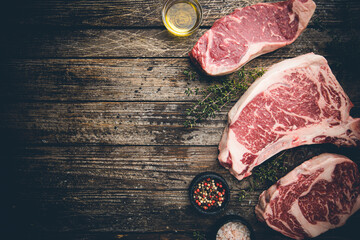 Wall Mural - Variety of Fresh Raw Black Angus Prime Meat Steaks T-bone, New York, Ribeye and seasoning on wooden background, top view