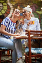 Wall Mural - Two female friends of different generations joking while they have a drink in the bar. Leisure, bar, friendship, outdoor