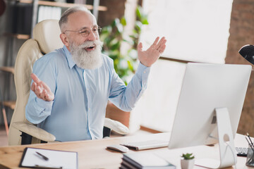 Photo of smiling funny age worker wear blue shirt spectacles communicating modern device indoors workshop workstation workplace