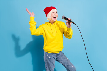 Sticker - Photo of funny adorable age woman dressed yellow sweatshirt red headwear singing karaoke isolated blue color background