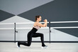Adult woman wearing tight black sportswear doing reverse lunge. Side view of fitnesswoman training legs with body weight in big hall with handrails. Sport, healthy lifestyle concept.