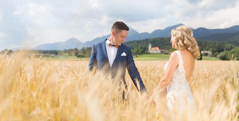 Wall Mural - Groom and bride holding hands in wheat field somewhere in Slovenian countryside.