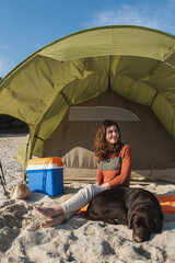 young smiling woman sitting on the sand next to her dog sleeping. cheerful female in a sunny day wit