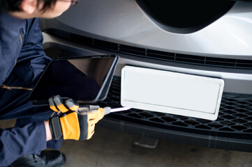 Wall Mural - Asian auto mechanic holding digital tablet checking car engine and license plate in auto service garage. Mechanical maintenance engineer working in automotive industry. Automobile servicing and repair