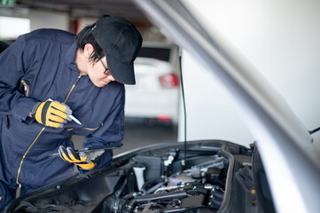 Wall Mural - Asian auto mechanic holding digital tablet checking car engine under the hood in auto service garage. Mechanical maintenance engineer working in automotive industry. Automobile servicing and repair