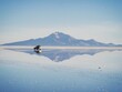 Offroad car SUV jeep of tour group on Salar de Uyuni salt flat lake in Bolivia andes mountains sunrise mirror reflection