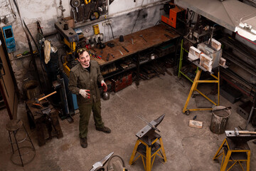 Wall Mural - Artisans portrait. Traditional metalworking process in a forge. Blacksmith in the workshop posing, top view.