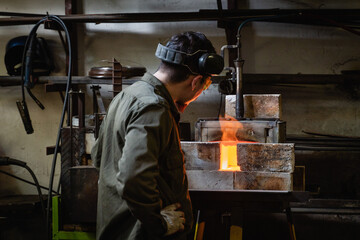 Canvas Print - Back view of a man in protective glasses watching the traditional process of heating metal