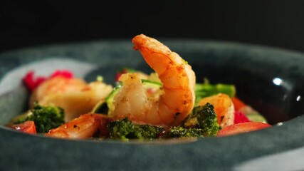 Wall Mural - Shrimp and vegetable salad in a black plate on a black background. Sea food. Restaurant menu.