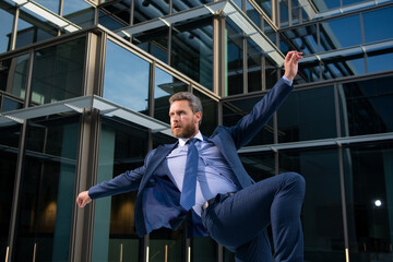 Excited businessman jumping outdoors on office building.