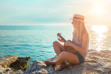 Summer Vacation. Smelling caucasian women relaxing and playing on ukulele on beach, so happy and luxury in holiday summer, outdoors sunset sky background. Travel and lifestyle Concept.
