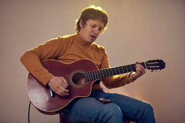 Male musician playing acoustic guitar on the amplifier in retro vintage room.