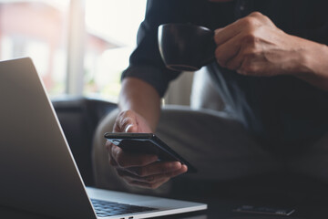 Wall Mural - Casual business man drinking coffee and using mobile phone during working on laptop computer at home