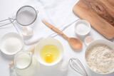 Fototapeta Pomosty - Frame of food ingredients for baking on a white background. Flour, eggs, sugar and milk in white and wooden bowls . Cooking and baking concept.