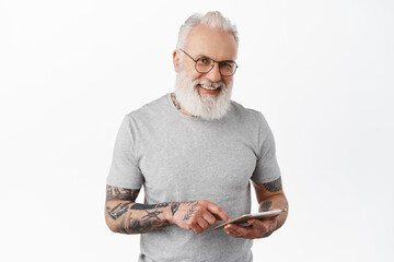 Smiling old man in glasses with tattoos, holding digital tablet, online shopping or networking, looking happy at camera, standing over white background