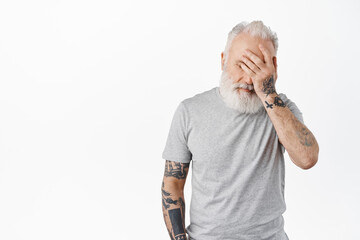 Oh gosh. Tired and annoyed senior man facepalm, hold hand on face distressed or exhausted, standing irritated in casual grey t-shirt against white background