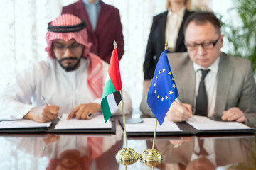 Poster - A person in a suit and tie and Arabian businessman signing documents by table
