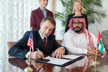 Poster - A group of people sitting by table while one of them signing contract after negotiation