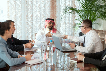 Poster - A group of people sitting around a table during discussion of documents